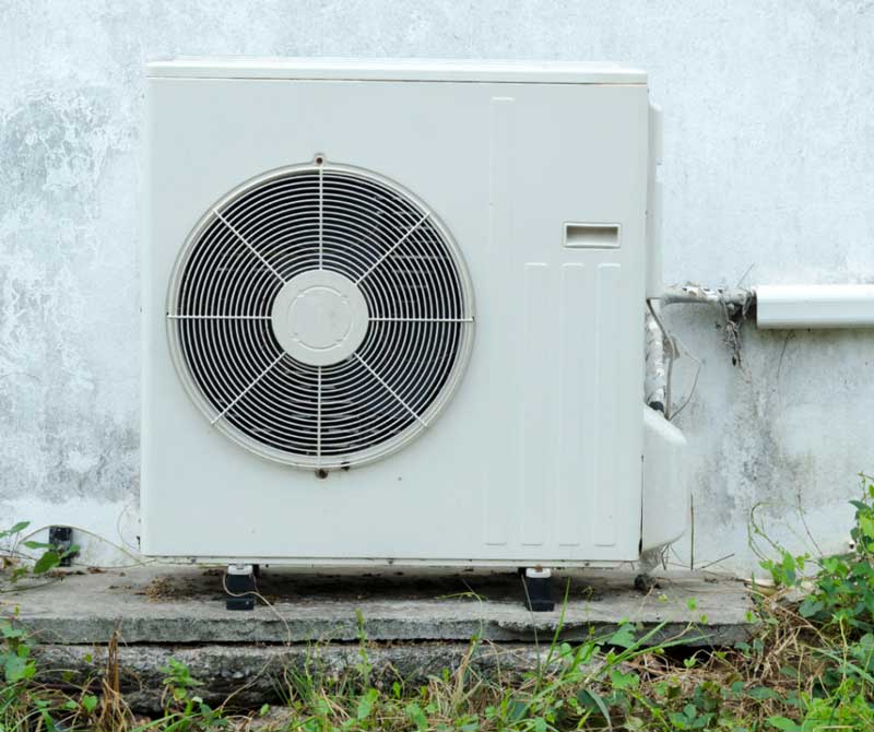 Outdoor air conditioning unit mounted on a concrete platform against a weathered wall.