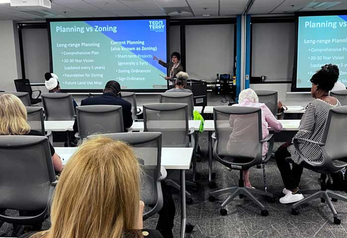 Classroom setting with a presenter discussing planning vs zoning; attendees sit facing a projection screen.