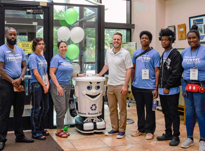Group photo with a recycling mascot and individuals wearing "Ted Terry Commissioner" shirts indoors.