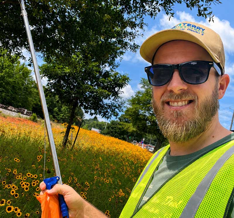 Commissioner Ted Terry in reflective vest in a field of wildflowers, smiling at the camera.