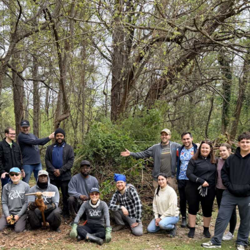 Group of people posing in a forest clearing, wearing casual outdoor attire, surrounded by trees and green foliage.