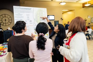 Four people engage in a discussion around a promotional poster for the Dekalb Farmers Market in a community setting.