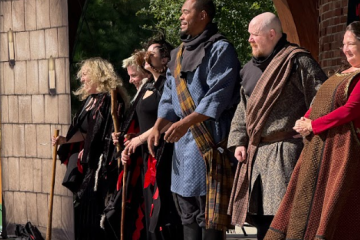 Group of actors in medieval costumes stand on an outdoor stage during a performance.